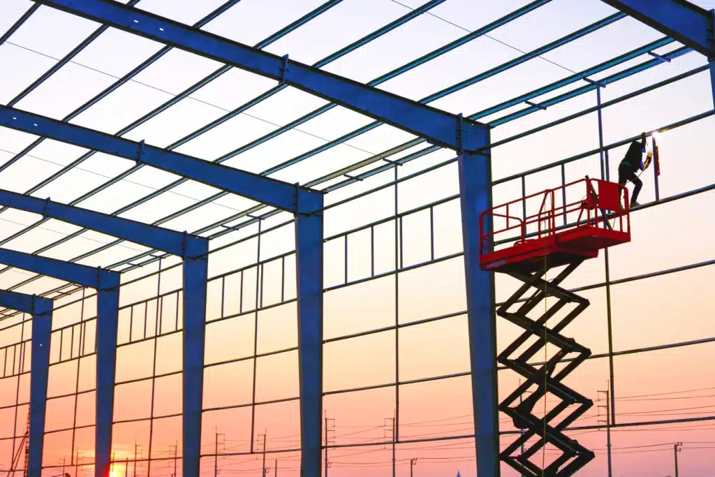 Soldador trabajando en construcción de estructura metálica para nave industrial al atardecer
