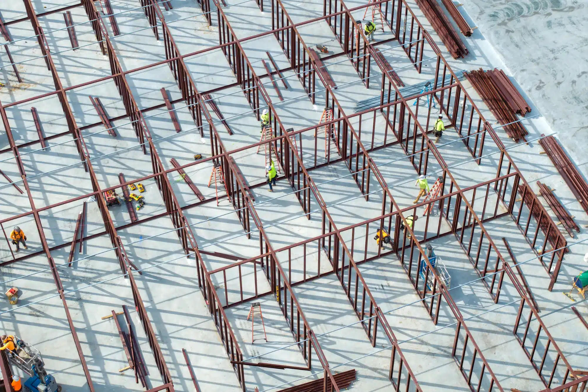 Vista aérea de construcción de estructura metálica industrial con equipo de operarios trabajando en obra