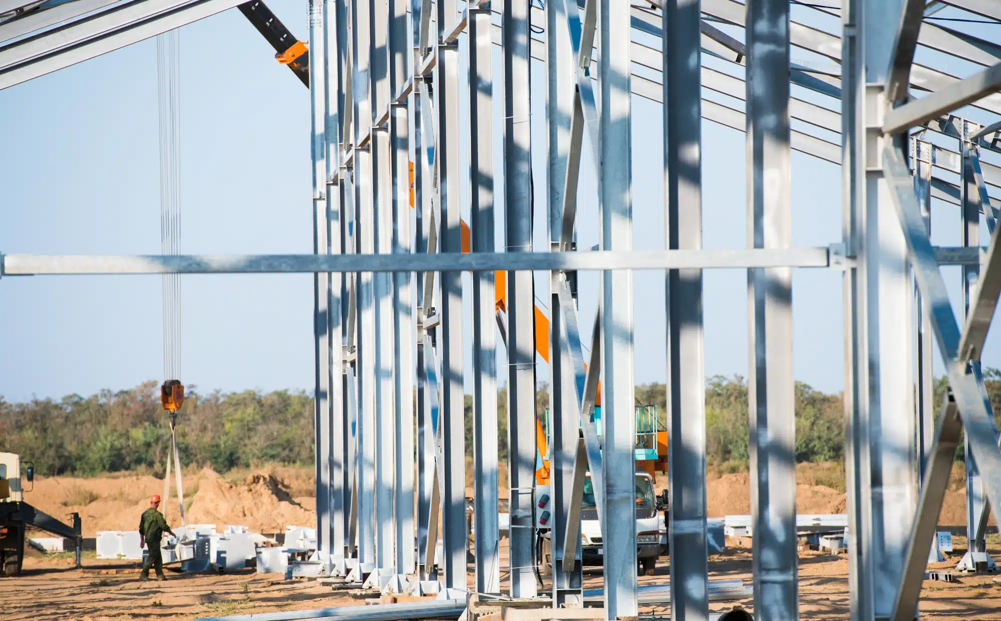 Operarios montando estructura metálica de acero en obra industrial con grúa