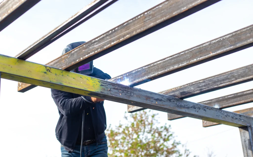 Soldador ejecutando soldadura puntual en perfilería de estructura metálica durante reparación en obra