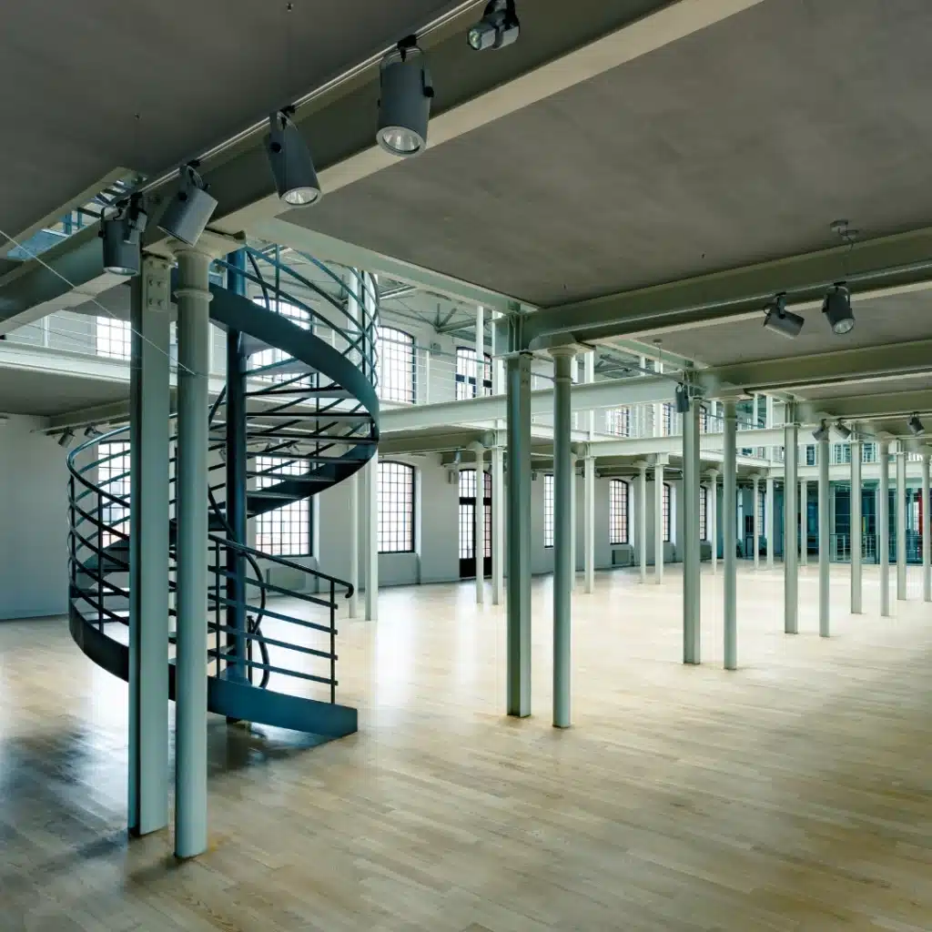 Escalera metálica de caracol instalada en nave industrial con entreplanta y estructura de pilares metálicos