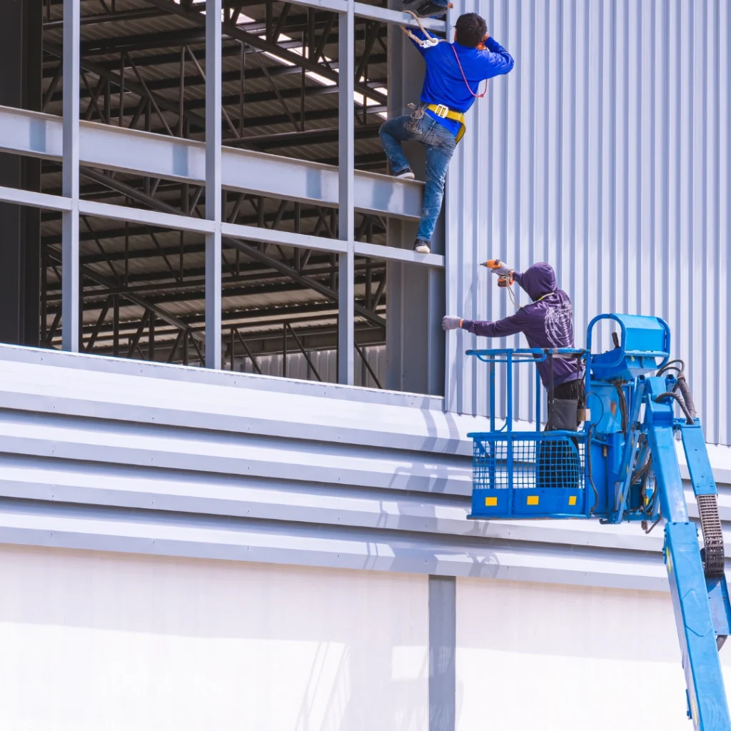 Montaje de panel metálico en fachada de nave industrial con plataforma elevadora y estructura de acero